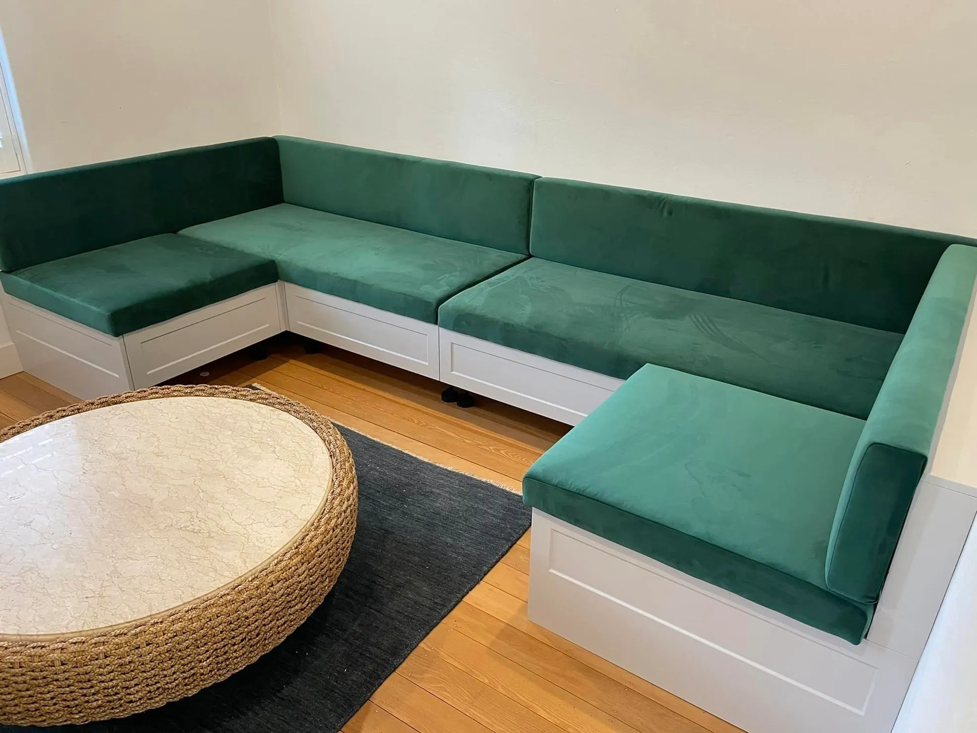 Custom built-in L-shaped banquette seating with green velvet cushions and white timber base