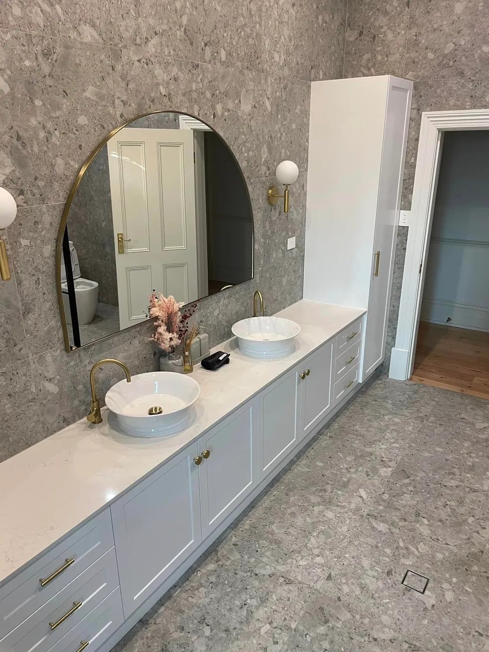 Dual bathroom vanity with vessel sinks, round gold mirrors and terrazzo feature wall