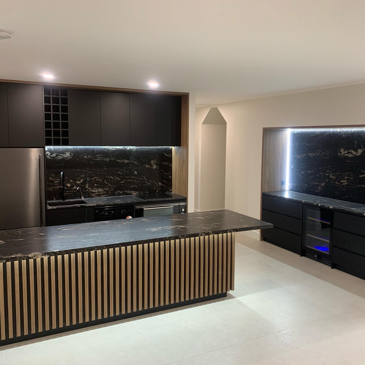 Dark matte black kitchen with marble benchtop and integrated wine fridge