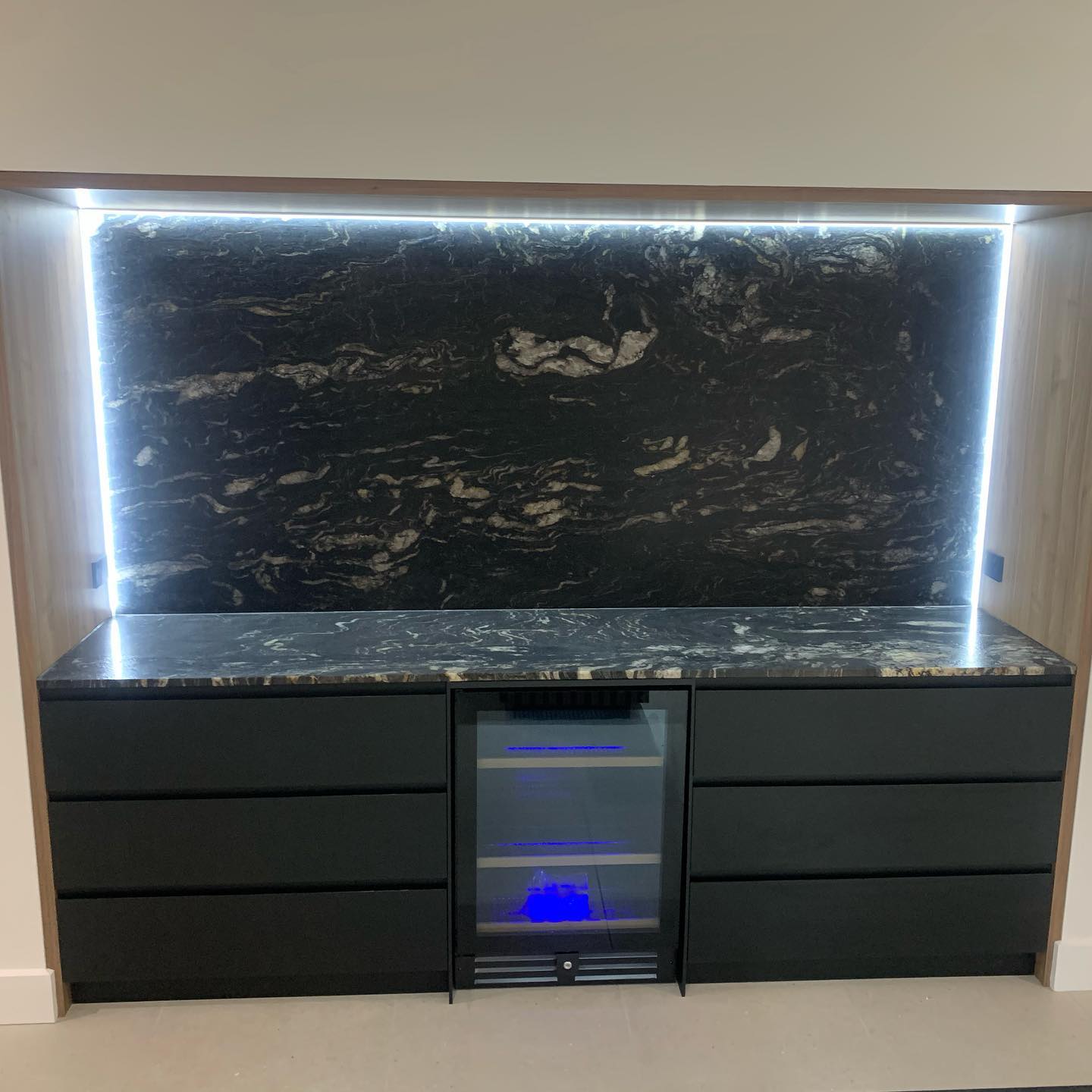 Custom bar unit with black marble benchtop and backlit stone feature wall
