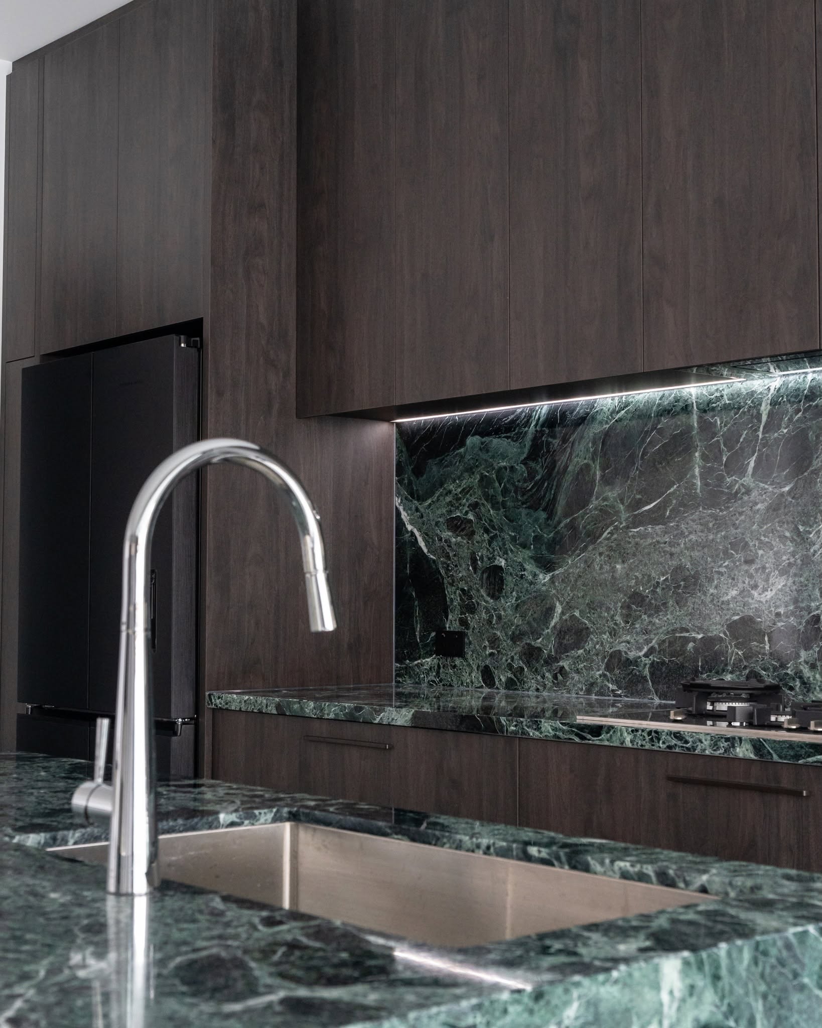 Dark stained timber kitchen with dramatic green marble benchtop and splashback